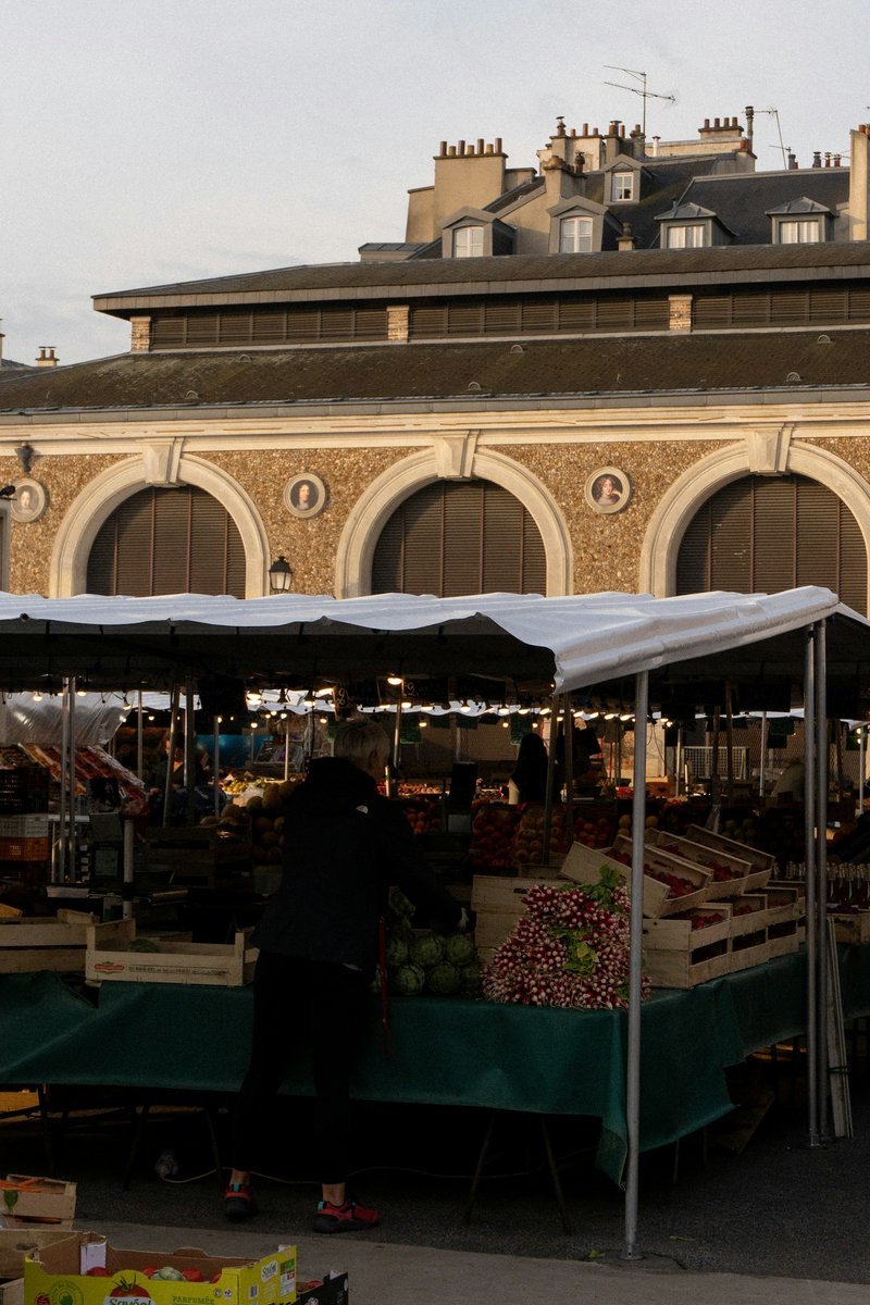Étals sous une bâche devant une halle de marché couvert à arcades
